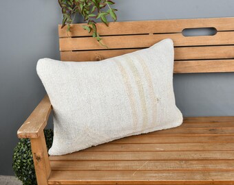 May include: A white throw pillow with subtle stripes sits on a wooden bench. The pillow is made of a soft, textured fabric.