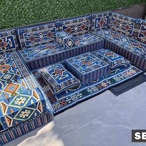 May include: A modular floor sofa set featuring blue fabric with intricate geometric patterns in orange, white, and black. The set includes rectangular floor cushions, backrests, and square pillows, all matching in design. The text SET 1 is visible.