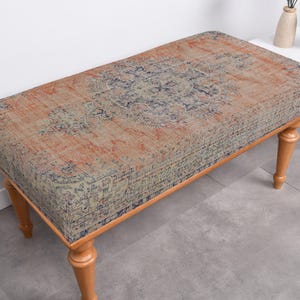 May include: A wooden bench with a patterned fabric seat. The fabric has a blue, orange, and green design. The bench has four legs.
