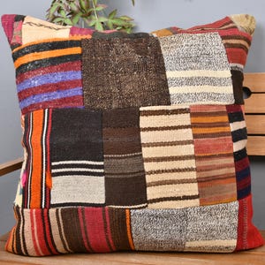 Può includere: Un cuscino quadrato patchwork con una varietà di colori e trame. Il cuscino presenta toppe rettangolari di tessuti marroni, beige, rossi, arancioni e neri. Il cuscino è appoggiato su una panca di legno.