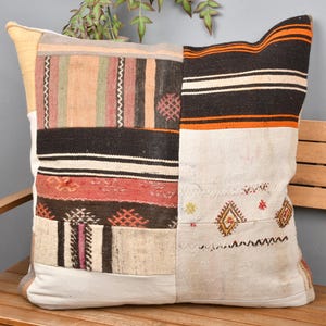 Puede incluir: Cojín cuadrado de patchwork con una variedad de colores y patrones. El cojín presenta secciones de telas beige, naranja, negras y rojas. Se coloca en un banco de madera con un fondo gris.