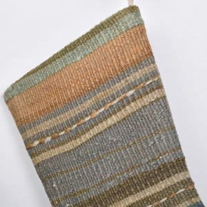 May include: Woven Christmas stocking with a striped pattern in shades of brown, green, and gray. The stocking is made of a textured fabric and has a loop for hanging. A festive holiday decoration.