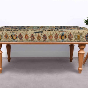 May include: A rectangular bench with a patterned top and wooden legs. The top features a beige background with a colourful, geometric design. The bench has four turned wooden legs, and is set against a white wall.