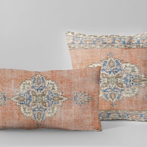 May include: Two decorative throw pillows with a vintage rug pattern. The pillows are rectangular and feature a repeating geometric design in shades of blue, cream, and orange on a rust-colored background.
