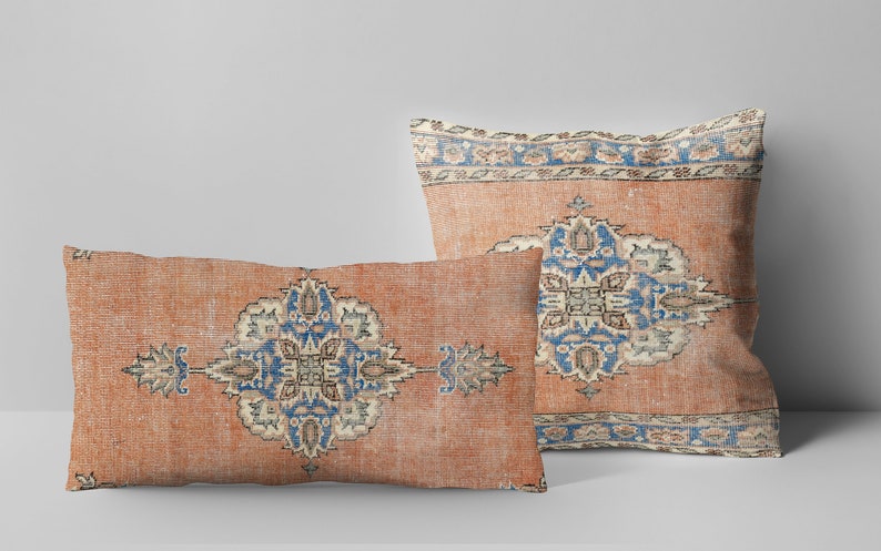 May include: Two decorative throw pillows with a vintage rug pattern. The pillows are rectangular and feature a repeating geometric design in shades of blue, cream, and orange on a rust-colored background.