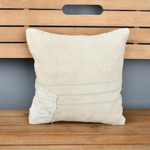 May include: A white throw pillow with blue stripes, made of a textured fabric. The pillow is sitting on a wooden bench.
