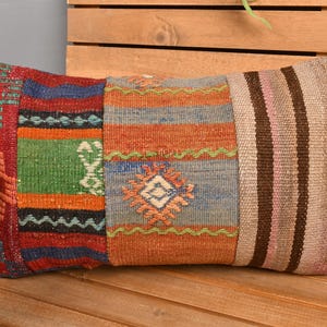 May include: Rectangular decorative pillow with a patchwork design. The pillow features sections of red, green, orange, and blue with geometric patterns and stripes. The pillow is placed on a wooden surface.