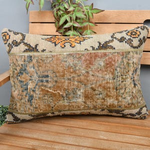 May include: A decorative pillow with a beige background and a brown, black, and orange geometric pattern. The pillow is made of a woven fabric and has a fringed edge.