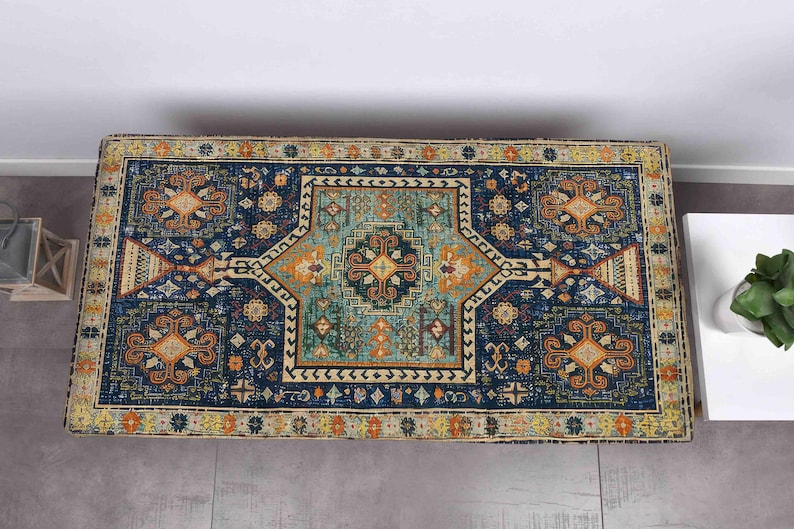 May include: A rectangular rug with a detailed geometric pattern. The rug has a dark blue base with teal, orange, and yellow elements. The design includes a central medallion and border details.