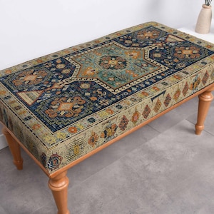 May include: A rectangular bench with a patterned top and wooden legs. The top features a detailed design in shades of blue, beige, orange, and teal, resembling a rug. The bench is supported by four light brown, slightly tapered legs.