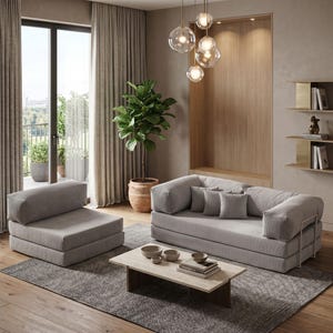 May include: A modern living room featuring a gray sofa, armchair, and coffee table. A large potted plant and a hanging light fixture with glass globes add to the room's contemporary design. The room has a neutral color palette with wooden floors and a patterned rug.