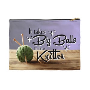 May include: A rectangular zippered pouch featuring a light purple and wood grain background. The text reads It takes Big Balls to be a Knitter, accompanied by a green yarn ball and two wooden knitting needles centered on the front.