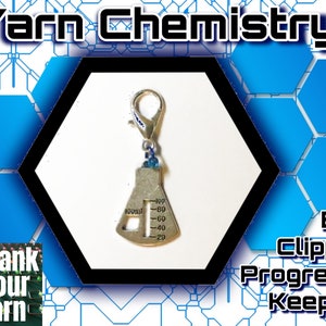 May include: Silver-toned yarn progress keeper shaped like a beaker with a blue bead and a silver clip. The beaker has a graduated scale marked in milliliters. The text "Yarn Chemistry!" is in the background.
