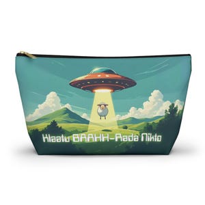 May include: A teal zippered pouch featuring a cartoon illustration of a UFO shining a light on a sheep. The background shows green hills, trees, and clouds. The text "Klaatu BAAHH-Rada Nikto" is printed on the pouch.