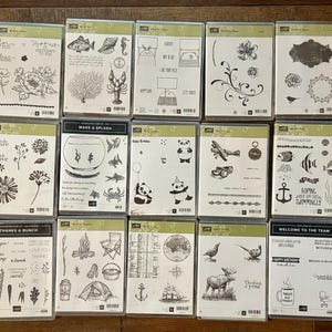 May include: A collection of clear stamp sets in plastic cases, featuring various designs such as flowers, animals, and text. The stamps are in black ink and are ideal for crafting and scrapbooking projects.