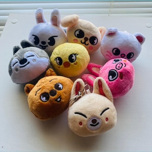May include: A collection of eight small, round plush keychain characters featuring various animal faces in colors including white, yellow, pink, brown, and gray. Each plush has embroidered facial features and a metal keychain attachment.
