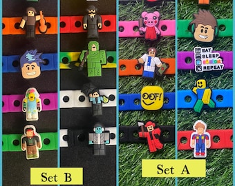May include: A collection of colourful silicone charm bracelets featuring various block-style character figures and icons. The charms include figures in diverse outfits, a yellow OOF square, and a square with the text EAT SLEEP ROBLOX REPEAT.