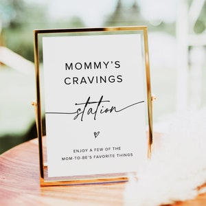 May include: A gold-framed sign with the text "MOMMY'S CRAVINGS station" and a heart symbol. The sign also includes the text "ENJOY A FEW OF THE MOM-TO-BE'S FAVORITE THINGS".