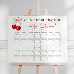 May include: A white sign on a wooden easel with the text "GUESS THE DUE DATE OF baby Jessica." The sign features a calendar grid with dates and a cherry illustration with a pink bow. The calendar is for a baby shower.