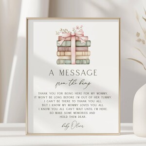 May include: A rectangular sign featuring a watercolor illustration of a stack of books tied with a pink ribbon and flowers. The text reads: A MESSAGE from the bump. THANK YOU FOR BEING HERE FOR MY MOMMY. IT WON'T BE LONG BEFORE I'M OUT OF HER TUMMY. I CAN'T BE THERE TO THANK YOU ALL, BUT I KNOW MY MOMMY LOVES YOU ALL. I KNOW YOU ALL CAN'T WAIT UNTIL I'M HERE. SO MAKE SOME MEMORIES AND HOLD THEM DEAR. baby Oliver.