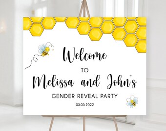 May include: A rectangular sign on a wooden easel featuring a yellow honeycomb pattern at the top. The text reads Welcome TO Melissa and John's GENDER REVEAL PARTY 03.05.2022. Two small cartoon bees are illustrated on the white background.