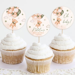 May include: Three cupcake toppers with a teddy bear holding balloons. The toppers are decorated with peach, green, and white balloons, clouds, and stars. The text on the toppers reads "Oh baby!" and "Natalie's Baby Shower 04.08.2023".