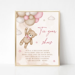 Puede incluir: Un oso de peluche rosa y marrón sujetando un montón de globos. El texto "Tie your shoes" está escrito en rosa. El texto de abajo dice "Place a balloon under your shirt and sit down. Bend over and tie your shoes. First person to tie both shoes without popping the balloon - wins!"