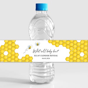 May include: Water bottle label with a honeycomb pattern and two cartoon bees. The text on the label reads "What will baby bee? Ella's Gender Reveal 04.05.2024".