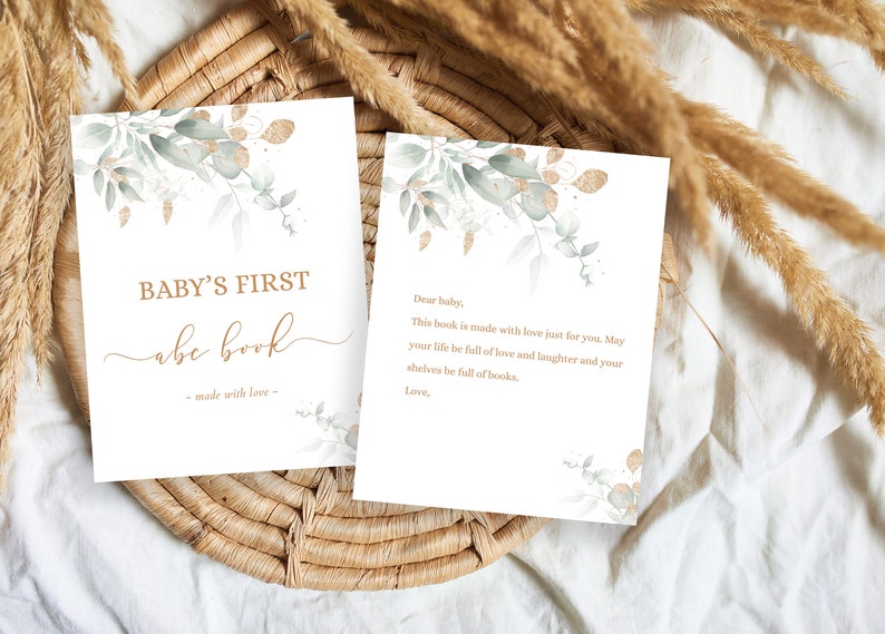 May include: Two cards with a watercolor design of green leaves and gold accents. The first card says "BABY'S FIRST abc book - made with love -." The second card says "Dear baby, This book is made with love just for you. May your life be full of love and laughter and your shelves be full of books. Love."