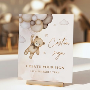 Puede incluir: Un letrero personalizado con una ilustración de un oso de peluche sosteniendo globos. El letrero tiene las palabras "Custom sign" y "Create your sign" en una fuente elegante. El letrero se muestra en un soporte dorado.