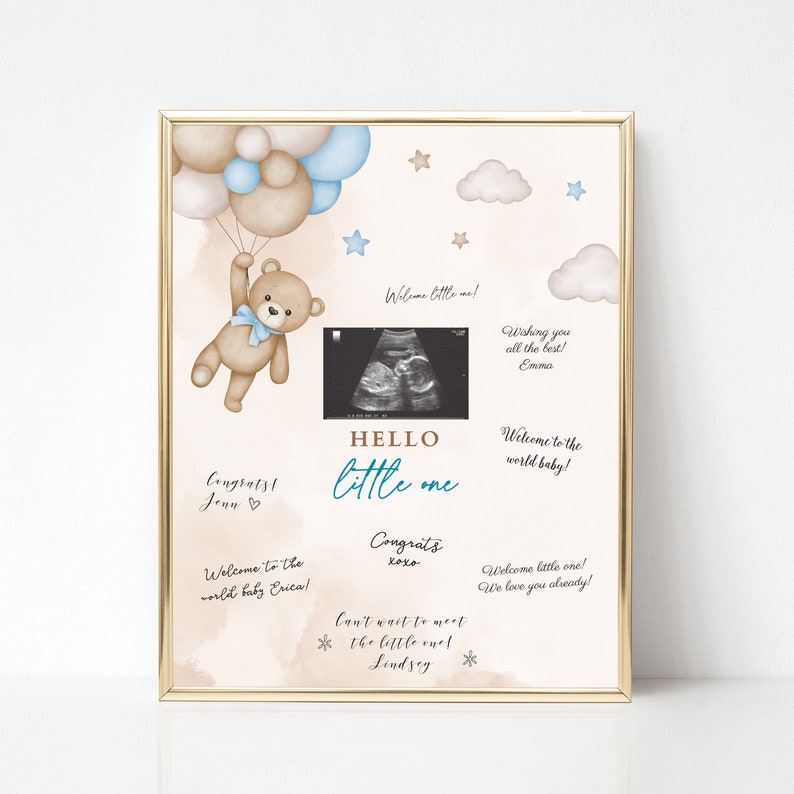 Puede incluir: Una impresi&oacute;n enmarcada con un borde dorado presenta un dise&ntilde;o de acuarela con un oso de peluche sosteniendo globos. El texto "HELLO little one" est&aacute; centrado debajo de una imagen de ultrasonido. Mensajes manuscritos y elementos decorativos completan el dise&ntilde;o.