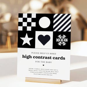 May include: A black and white high contrast card for babies, featuring geometric shapes and patterns. The card includes a star, heart, snowflake, circle, diagonal stripes, and a checkerboard pattern. Text on the card reads "PLEASE HELP US MAKE high contrast cards FOR THE BABY."