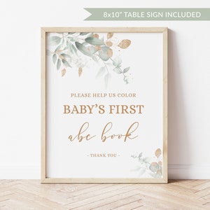May include: A white 8x10 inch table sign with a gold and green floral design. The sign says "Please help us color baby's first abc book - Thank you -"