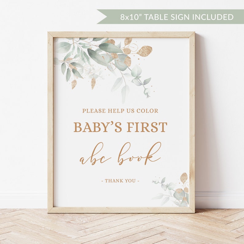 May include: A white 8x10 inch table sign with a gold and green floral design. The sign says "Please help us color baby's first abc book - Thank you -"