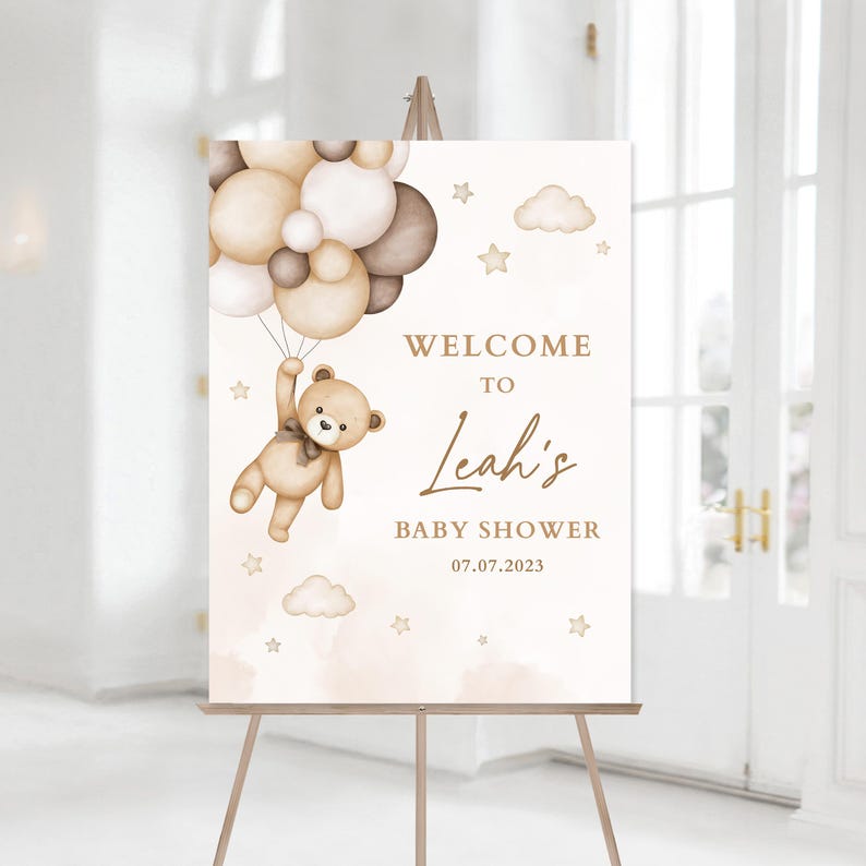 May include: Welcome to Leah's Baby Shower sign featuring a teddy bear holding balloons in the sky. The sign is on a wooden easel and has a watercolour background with clouds and stars.