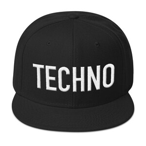 Op de afbeelding: Zwarte baseballcap met het witte woord "TECHNO" geborduurd op de voorkant. De cap heeft een platte klep en een gestructureerde pasvorm. Een klassieke hoed.