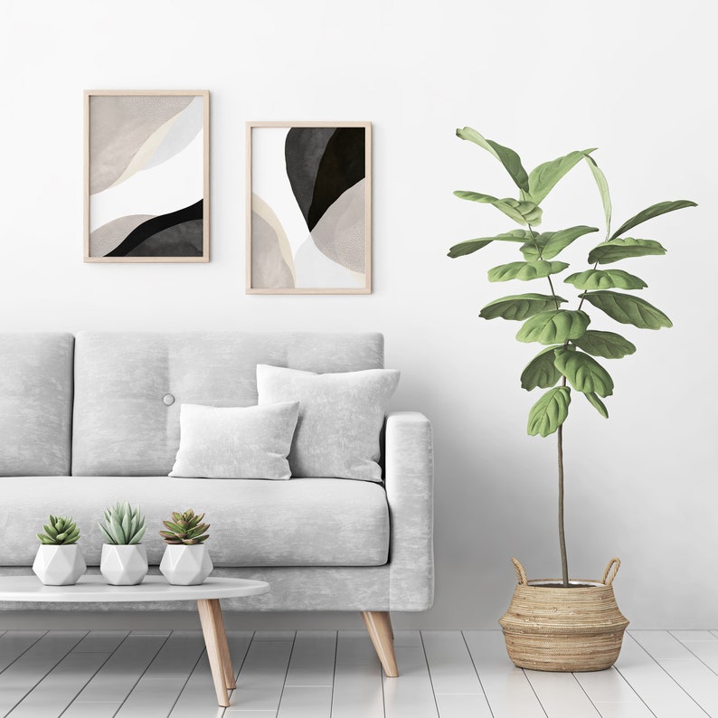 May include: A white sofa with two pillows and three small potted succulents sits in front of a white wall with two framed abstract art prints. A large potted plant with green leaves sits on the right side of the image.