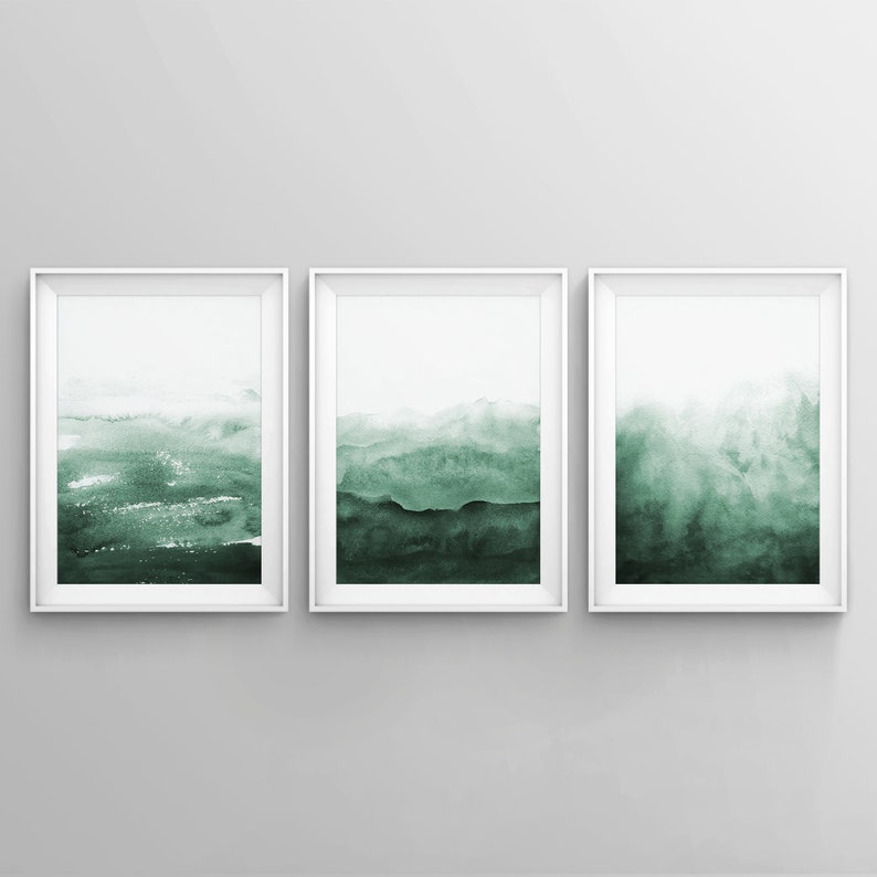 May include: Three framed watercolor paintings with a green and white abstract landscape design. The paintings are in white frames and are hung on a white wall.