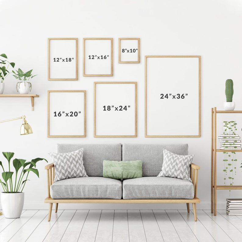 May include: A white wall with a sofa and five framed pictures of different sizes. The pictures are all in wooden frames and have measurements written on them in inches. The sofa is grey with two cushions and is sitting on a wooden floor.