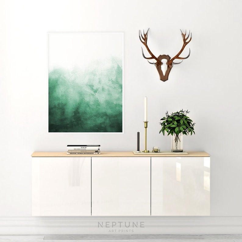 Puede incluir: Un armario blanco con tres puertas, una tapa de madera y una impresi&oacute;n de acuarela verde colgada en la pared encima. Un juego de libros y un candelero dorado est&aacute;n en la parte superior del armario. Una montura de asta de ciervo est&aacute; en la pared a la derecha de la impresi&oacute;n. Una planta en maceta est&aacute; en el armario.