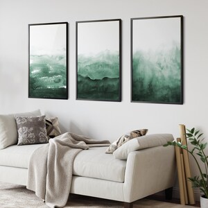 May include: Three framed abstract watercolor paintings with a green and white color scheme. The paintings are hung on a white wall above a white couch.