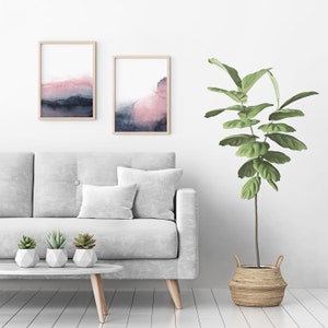 May include: A white sofa with two cushions and three small potted plants on a coffee table in front of it. Two framed abstract watercolour paintings hang on the wall behind the sofa. A large potted plant with green leaves stands to the right of the sofa.
