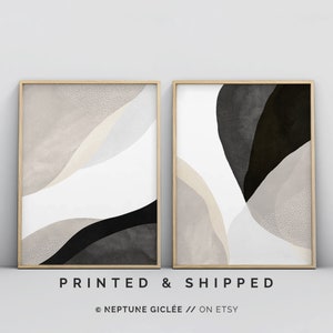 May include: Two abstract art prints in wooden frames. The prints feature a white background with black and beige abstract shapes. The left print has a white background with black and beige abstract shapes. The right print has a white background with black and beige abstract shapes.