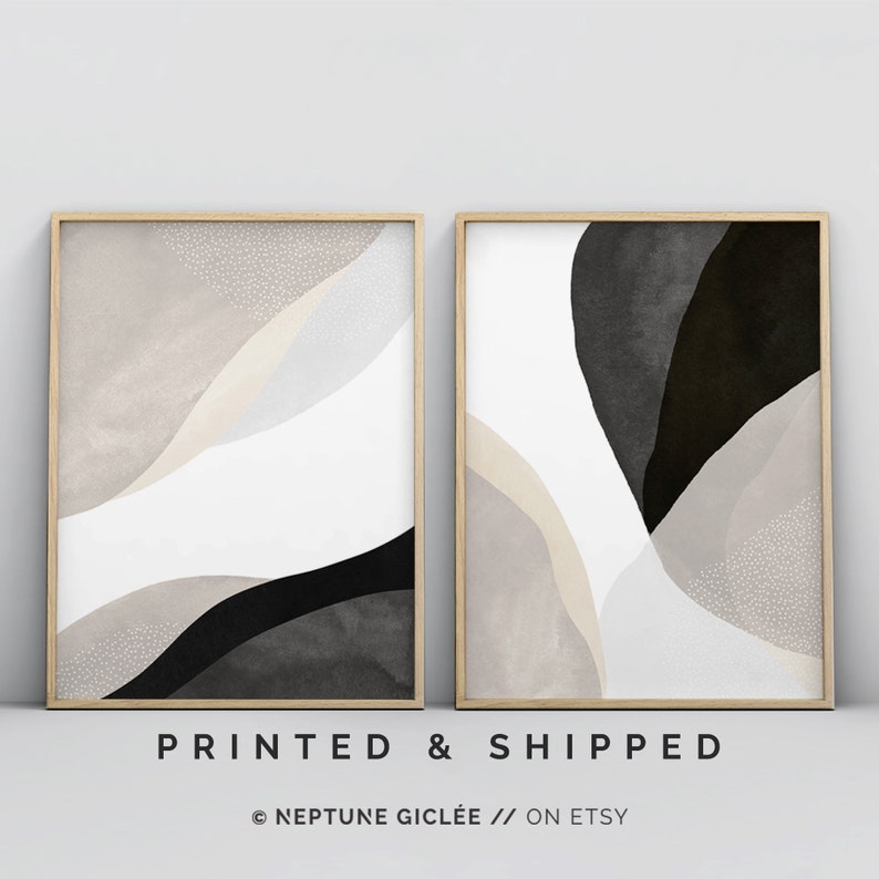 May include: Two abstract art prints in wooden frames. The prints feature a white background with black and beige abstract shapes. The left print has a white background with black and beige abstract shapes. The right print has a white background with black and beige abstract shapes.