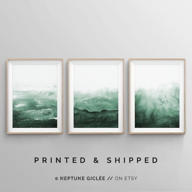 May include: Set of three framed watercolor prints with a green and white abstract landscape design. The prints are in wooden frames and are arranged in a row.