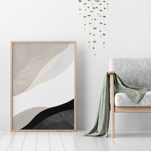 May include: A framed abstract print with beige, white, and black watercolor-like shapes. The print is hanging on a white wall next to a light gray armchair with a green throw blanket.