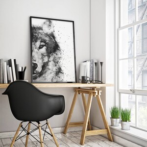 Op de afbeelding: Zwart-witte aquarelverf van een wolvenkop, ingelijst en hangend aan een witte muur boven een houten bureau met een zwarte stoel en planten.