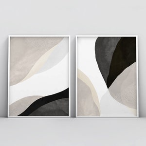 May include: Two framed abstract art prints with white frames. The prints feature a black and white abstract design with beige and gray accents.