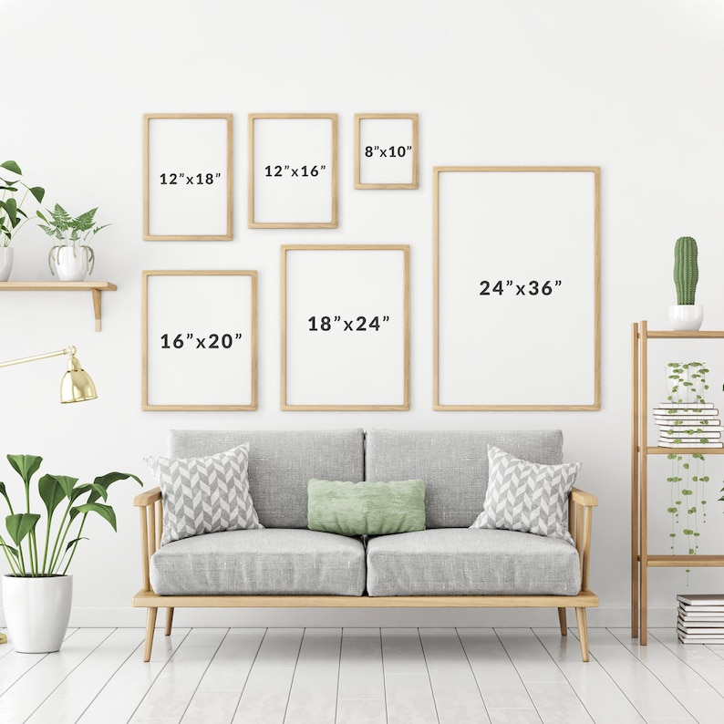 May include: A white wall with a couch and five framed pictures of different sizes. The pictures are all in wooden frames and have measurements written on them in inches. The couch is gray with two pillows and is sitting on a wooden floor.
