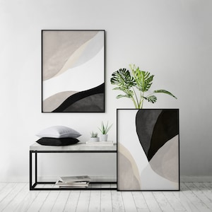 May include: Two black framed abstract art prints with beige, white, and black colors. The prints are hanging on a white wall above a black metal table with a concrete top. A small potted plant is on the table in front of the prints.